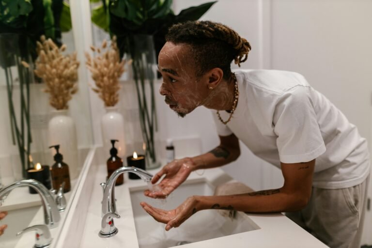 Man washing face in bathroom sink, showcasing a morning skincare routine for hygiene.